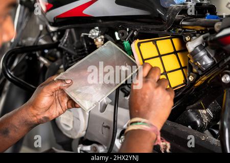 Primo piano del meccanico impegnato a fissare il filtro dell'aria della motocicletta in garage - concetto di servizio di riparazione e manutenzione. Foto Stock