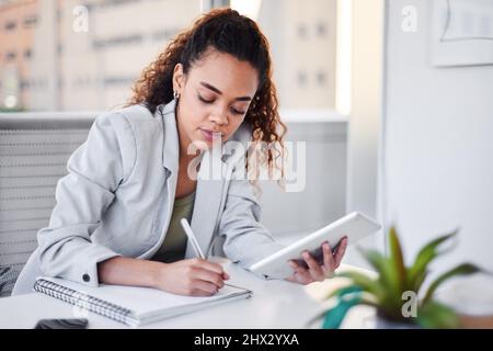 Una giovane donna d'affari scrive appunti in un notebook dal suo tablet digitale Foto Stock