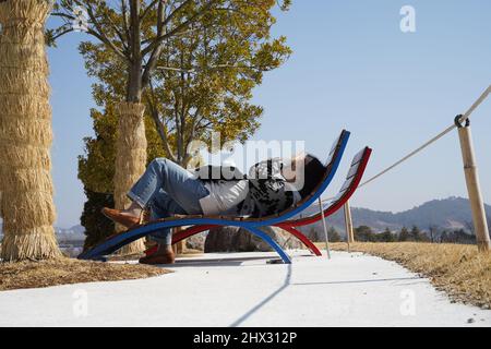 È una panchina posta sotto alcuni alberi, ma è difficile aprire gli occhi perché il sole splende sul viso. Foto Stock