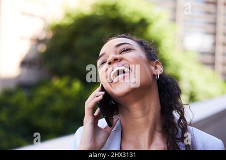 Una giovane donna ride felicemente durante una conversazione sul suo cellulare Foto Stock