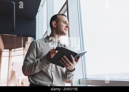 Lavorare con la carta. Serio imprenditore maschile che lavora in ufficio da solo, leggere documento in copia cartacea, pensare a termini. Il giovane uomo messo a fuoco che fa paperwo Foto Stock