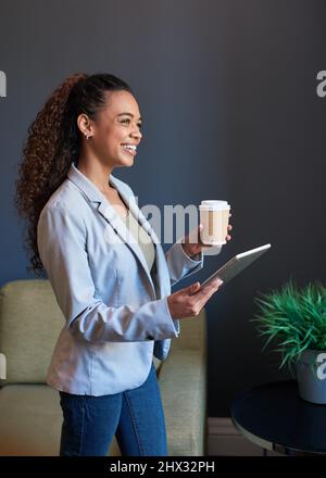 Una giovane donna si alza con il suo caffè e tablet digitale preparati per la giornata Foto Stock