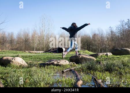 Una giovane ragazza cammina su pietre a passo su un percorso di ostacoli in un parco, al sole della sorgente luminosa, in una foresta a Diemen, nei Paesi Bassi. Foto Stock