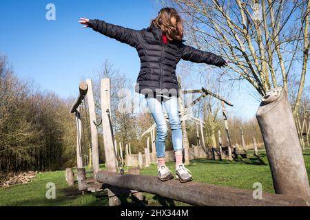 Una giovane ragazza cammina lungo una trave di legno su un percorso ad ostacoli in un parco, al sole della sorgente luminosa, in una foresta a Diemen, nei Paesi Bassi. Foto Stock