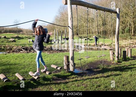 Una giovane ragazza si fa strada attraverso un percorso di ostacoli in un parco, nel sole della sorgente luminosa, in una foresta a Diemen, nei Paesi Bassi. Foto Stock