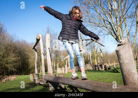 Una giovane ragazza si bilancia su un fascio di legno su un percorso di ostacoli in un parco, al sole della sorgente luminosa, in una foresta a Diemen, nei Paesi Bassi. Foto Stock