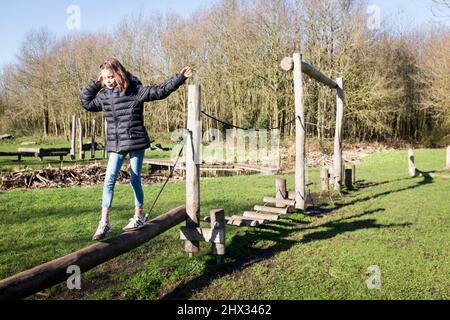 Una giovane ragazza si bilancia su un fascio di legno su un percorso di ostacoli in un parco, al sole della sorgente luminosa, in una foresta a Diemen, nei Paesi Bassi. Foto Stock