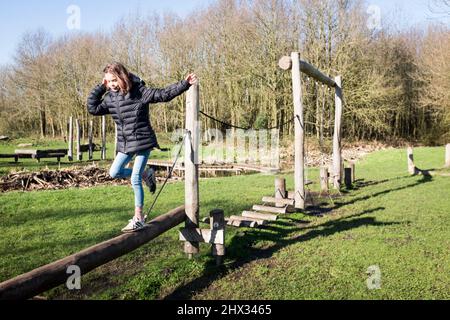 Una giovane ragazza si stende lungo un raggio di legno su un percorso ad ostacoli in un parco, al sole della sorgente luminosa, in una foresta a Diemen, nei Paesi Bassi. Foto Stock