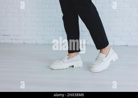 Gambe di una giovane bella donna in pantaloni neri e moderni eleganti loafer in pelle bianca. Nuova collezione di scarpe da donna primavera-estate 2022 Foto Stock