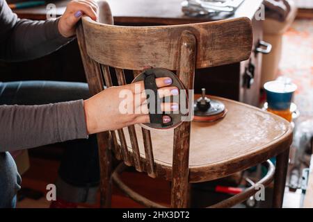 Primo piano di rimozione del vecchio strato di vernice levigatura sedia invecchiata con pezzo di carta vetrata speciale in officina per la ristrutturazione dei mobili. Pratiche sostenibili Foto Stock