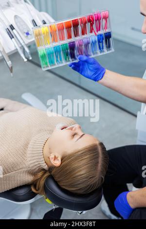 Il medico mostra delle fasce elastiche colorate sulle bretelle del paziente. Uomo con bretelle in filo sui denti sottoposti ad una procedura dentale presso la clinica. Dentis Foto Stock