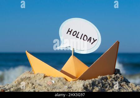 Orange Paper Boat su Sandy Seashore Close-up. Piccola barca da carta Foto Stock