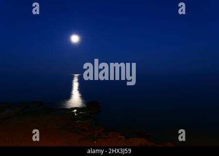 Una luna piena brilla sul mare in una notte d'estate. Paesaggio notturno con luna e moonbeam nel mare. Foto Stock