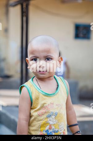 Un ragazzo giovane e carino con testa rasata che indossa una maglia di gilet Popeye gialla sbiadita a Mahalaxmi Dhobi Ghat, una grande lavanderia all'aperto a Mumbai, India Foto Stock