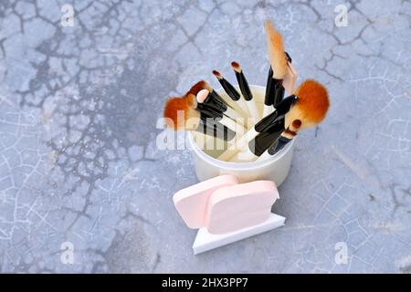 closeup il mazzo bianco marrone makeup kit spazzola con spugne palla nella scatola di plastica su sfondo grigio marrone fuori fuoco. Foto Stock