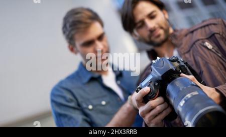 Due amici che parlano delle loro fotografie. Inquadratura a basso angolo di due uomini che guardano lo schermo lcd di una fotocamera digitale. Foto Stock