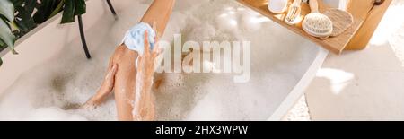 Vista ad alto angolo della giovane donna con spugna mentre si fa il bagno, rilassante in vasca da bagno piena di bolle Foto Stock