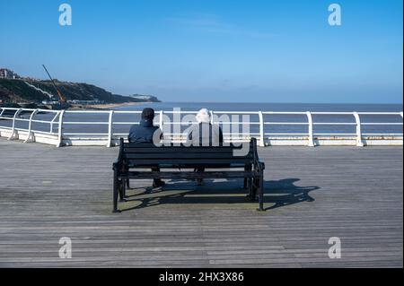 Persone anziane sedute su una panchina su un molo di Norfolk al sole d'inverno Foto Stock