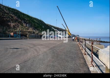 Cromer Norfolk Promenade con cani a piedi e due grandi gru che lavorano sui gradini della scogliera Foto Stock