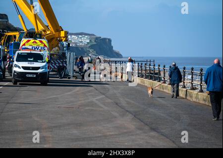 Cromer Norfolk Promenade con cani a piedi e due grandi gru che lavorano sui gradini della scogliera Foto Stock