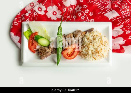 Grigliate turche SIS agnello Kebab con riso e insalata in un piatto isolato su colorato tavolo panno vista dall'alto su sfondo grigio Foto Stock