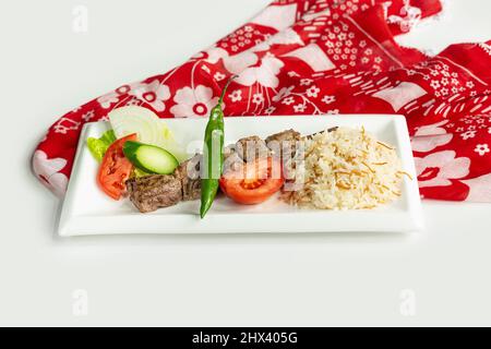 Grigliate turche SIS agnello Kebab con riso e insalata in un piatto isolato su colorato tavolo panno vista dall'alto su sfondo grigio Foto Stock