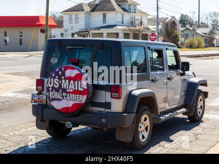 GASTONIA, NC, USA-3 MARZO 2022: Modello ritardato Jeep Wrangler con copertura posteriore di pneumatico che dichiara 'US Mail Rural Carrier' su sfondo American Flag. Foto Stock