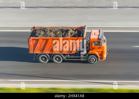 Lo scarico del dumper con un carico di terreno nel cassone procede ad alta velocità su strada Foto Stock
