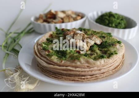 Pane piatto indiano cosparso di condimento all'aglio verde e servito con formaggio casereccio saltato. Scatto su sfondo bianco. Foto Stock