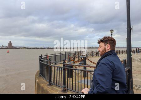 Giovane uomo con capelli favolosi che si affacciano sul mare, guardando verso Wirral da Liverpool Foto Stock