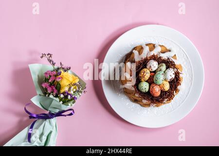 Vista dall'alto della torta di Pasqua su sfondo rosa. Con uova colorate poste in un nido di cioccolato sulla parte superiore Foto Stock