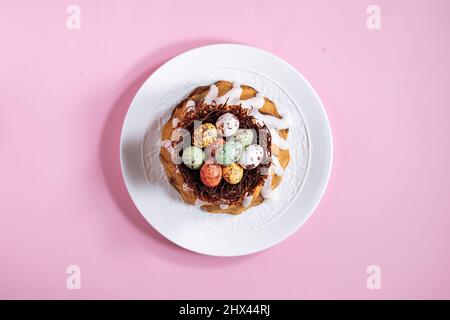 Vista dall'alto della torta di Pasqua su sfondo rosa. Con uova colorate poste in un nido di cioccolato sulla parte superiore Foto Stock