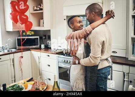 Ti amo tanto. Scatto corto di una giovane coppia affettuosa che abbraccia mentre prepara la cena nella loro cucina. Foto Stock
