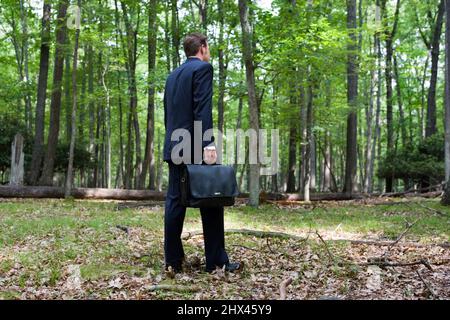 GIOVANE UOMO D'AFFARI CON VALIGETTA IN PIEDI DA SOLO NELLO SGOMBERO DI FORESTA SETTENTRIONALE MISTA TEMPERATA Foto Stock