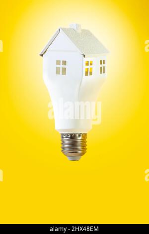 Lampadina a bulbo levitating nella forma di una casa bianca, isolata su sfondo giallo. Lampadina a forma di casa Foto Stock