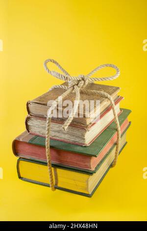 4 libri impilati legati con una corda di iuta levitating su sfondo giallo Foto Stock