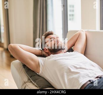 Niente di più rinfrescante di un pisolino pomeridiano. Scatto corto di un giovane uomo che prende un pisolino su un divano a casa. Foto Stock