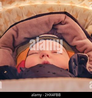 Un bambino nei vestiti di inverno dorme sdraiato in una carrozza del bambino, primo piano del viso, età 8 mesi Foto Stock