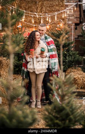 Una bella giovane coppia in abiti bianchi è seduta vicino ad un albero di Natale nel giardino. Felice uomo e donna, romanticismo, festa di Natale, divertimento, l Foto Stock