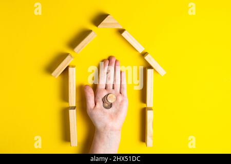 Vista dall'alto della mano del bambino close up blocchi di costruzione che mostrano soldi mince, casa, capanna di legno Foto Stock
