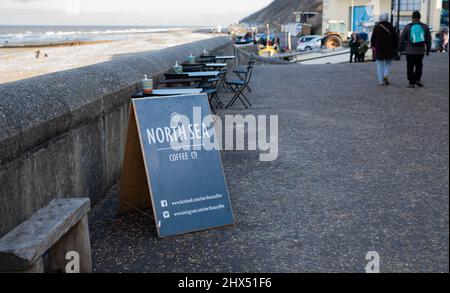 Cartello North Sea Coffee Shop di fronte ai tavoli all'aperto sulla spianata nella cittadina balneare di Cromer sulla costa nord del Norfolk Foto Stock
