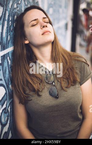 Giovane e bella donna si appoggia contro un muro colorato e si pone per la macchina fotografica - stile di strada tipico Foto Stock