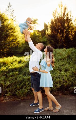 Felice famiglia amorevole con bella bambina al parco, forte ascensore papà in aria sorridente figlia, i genitori giocare con il bambino, bella moglie abbraccio cura h Foto Stock