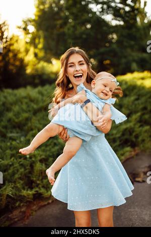 Donna overjoyed giocare con bella bambina al parco, adorabile madre tenere la bambina in braccia, sorriso, godere di momenti di famiglia felice, outdo fine settimana Foto Stock