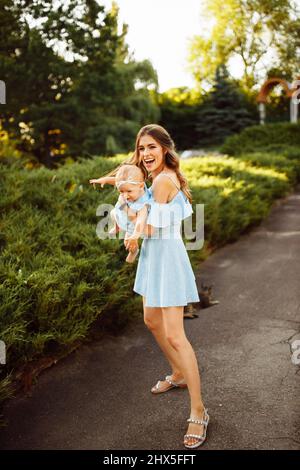 Donna overjoyed giocare con bella bambina al parco, adorabile madre tenere la bambina in braccia, sorriso, godere di momenti di famiglia felice, outdo fine settimana Foto Stock