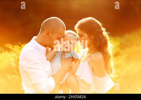 Bella mamma e papà con bella figlia al parco, i giovani genitori tenere carina bambina in braccia teneri, sorriso, godersi i momenti felici della famiglia Foto Stock