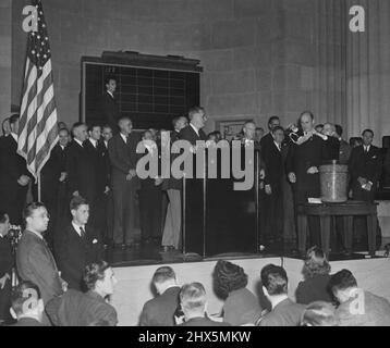 Il Segretario Morganthau disegna numero -- Segretario del Tesoro Henry Morganthau, Jr., essendo stato bendato prima di disegnare il secondo numero della lotteria di progetto tenuta a Washington il 29th ottobre. Il colonnello Charles R. Morris sta applicando la cieca mentre il presidente Franklin D. Roosevelt guarda sopra dallo stand dell'oratore. Il primo numero disegnato, 158, è postato sulla lavagna in background. Ottobre 29, 1940. (Foto di ACME). Foto Stock