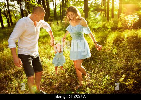 I genitori allegri giocano con la bambina, sorridendo, sorridendo il padre e la mamma sollevano in aria cute toddler, la giovane famiglia che cammina al parco, godono felice Foto Stock