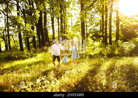 I genitori molto gioiosi giocano con la bambina, il papà attento e la mamma bella ascensore in aria adorabile bambina, la famiglia giovane a piedi al parco, godere felice Foto Stock