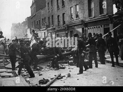 Disordini a Londra dopo la marcia fascista bandita -- Londra orientale è stata teatro di molti disordini ieri, quando migliaia di persone si sono riunite per protestare contro la marcia fascista proposta, che è stata alla fine bandita dalla polizia. sono stati effettuati 84 arresti. I poliziotti della foto smantellano una barriera che è stata eretta dai dimostranti nelle vicinanze di Aldgate, E. si noti il camion rovesciato. Ottobre 4, 1936. (Foto di Topical Press).;rivolte a Londra dopo il divieto di marcia fascista -- East London è stata la scena di molte rivolte Foto Stock